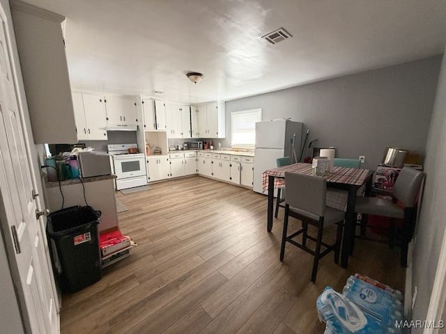 kitchen with extractor fan, white cabinets, light wood-type flooring, and white appliances