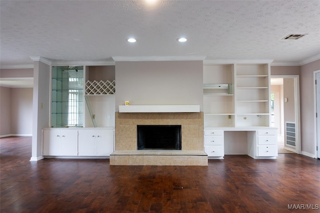 unfurnished living room featuring a tiled fireplace, built in desk, dark hardwood / wood-style flooring, and a textured ceiling