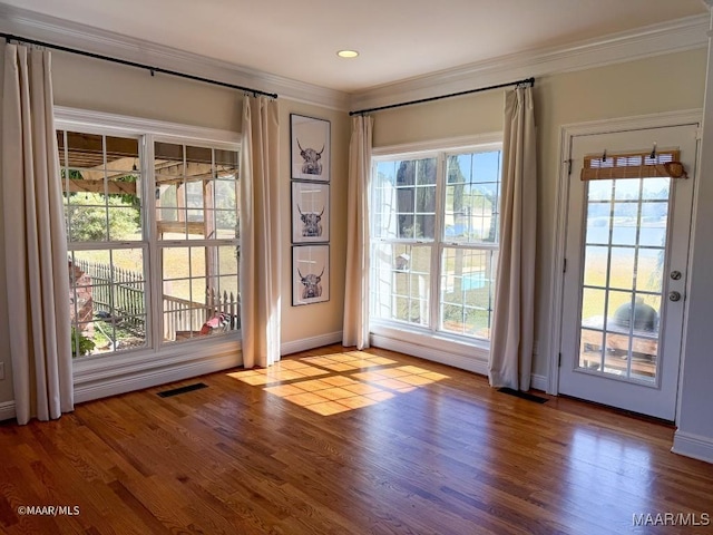 doorway featuring wood finished floors, visible vents, ornamental molding, and baseboards