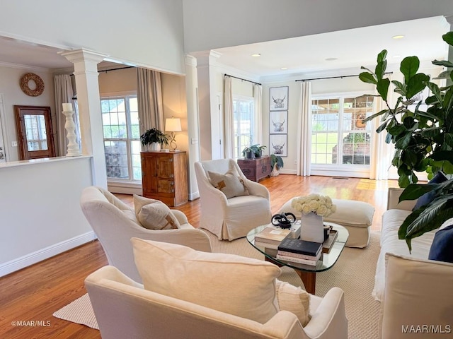living room with wood finished floors, crown molding, baseboards, and decorative columns