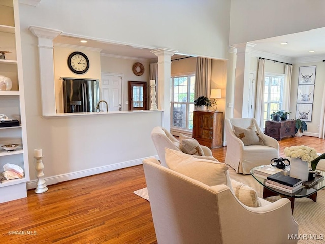 living area featuring ornate columns, wood finished floors, and crown molding