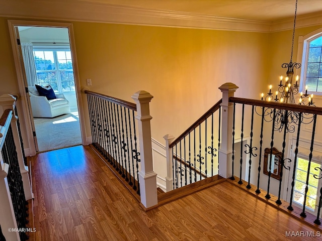 stairs with wood-type flooring, crown molding, and a notable chandelier