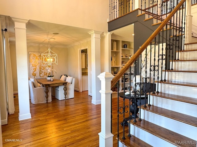 stairs with an inviting chandelier, built in features, hardwood / wood-style flooring, and ornamental molding