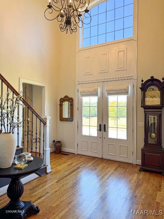 entrance foyer featuring a chandelier, french doors, a towering ceiling, and wood-type flooring