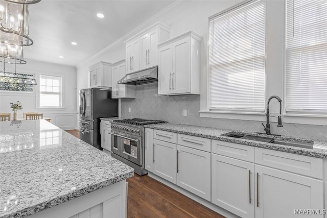 kitchen with white cabinets, a sink, a chandelier, under cabinet range hood, and appliances with stainless steel finishes