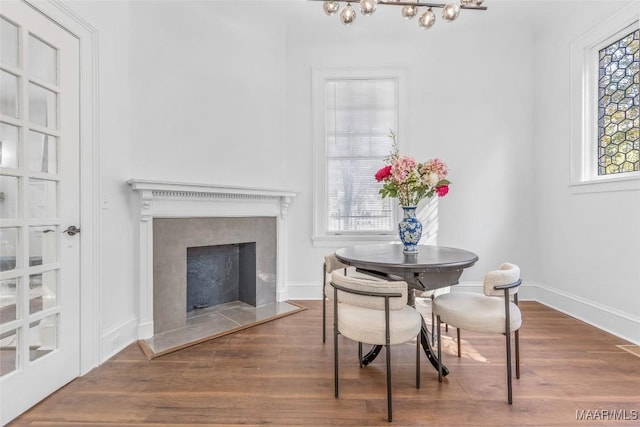 dining space featuring baseboards, wood finished floors, a fireplace, and a notable chandelier