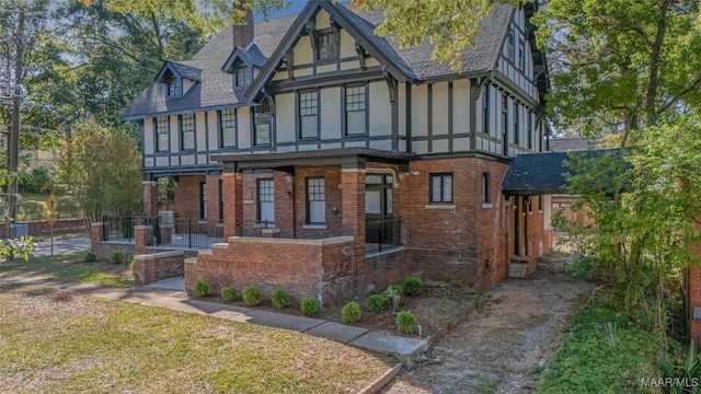 rear view of house featuring a porch, a chimney, brick siding, a shingled roof, and stucco siding