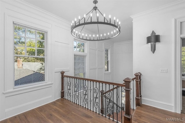 corridor with wood finished floors, an inviting chandelier, an upstairs landing, and crown molding