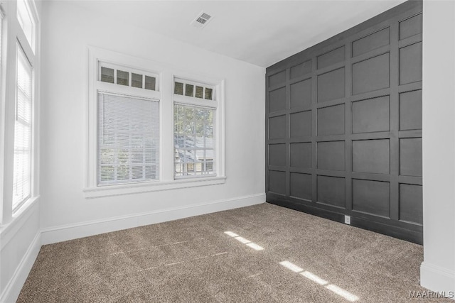 empty room featuring baseboards, visible vents, carpet floors, and a decorative wall