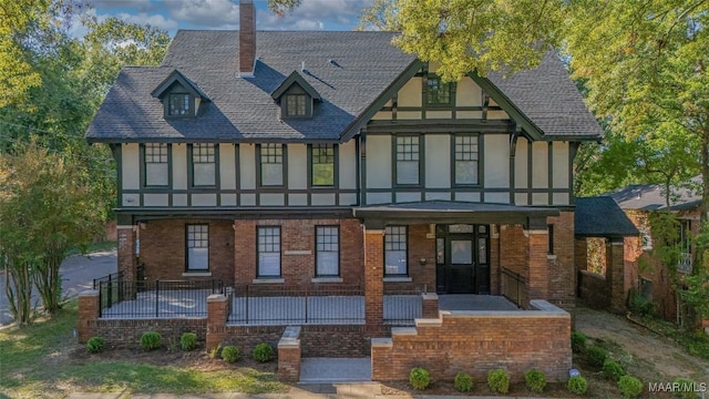 back of property with brick siding, covered porch, roof with shingles, and stucco siding