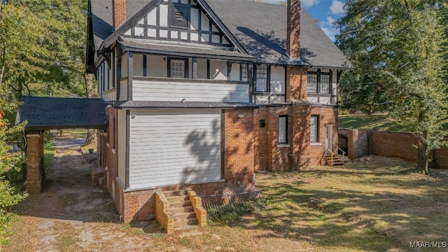 back of house with an attached carport, a chimney, brick siding, entry steps, and a balcony