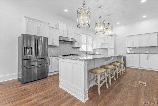 kitchen featuring tasteful backsplash, a chandelier, appliances with stainless steel finishes, under cabinet range hood, and dark wood-type flooring