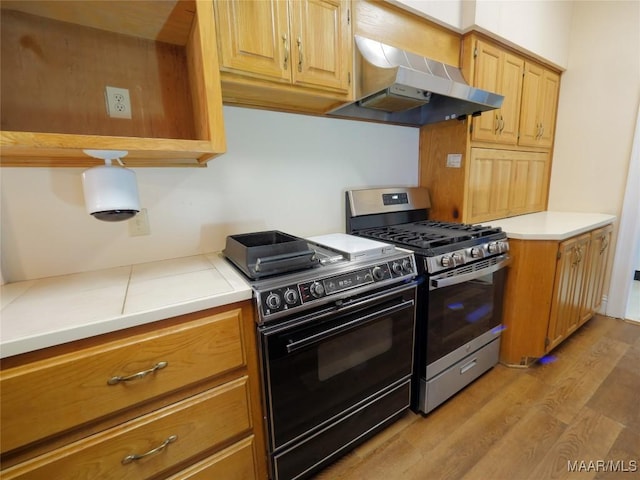kitchen with black electric range, gas stove, light wood-style flooring, light countertops, and range hood