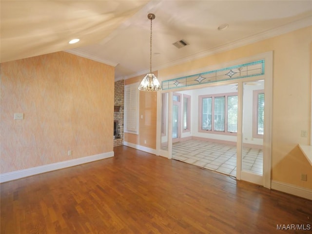 unfurnished dining area featuring wood finished floors, ornamental molding, a chandelier, a brick fireplace, and baseboards