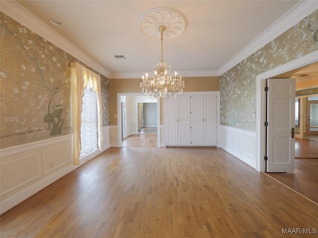unfurnished dining area with wallpapered walls, a decorative wall, a wainscoted wall, and a notable chandelier