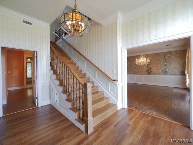 stairs with a towering ceiling, a notable chandelier, hardwood / wood-style flooring, and ornamental molding