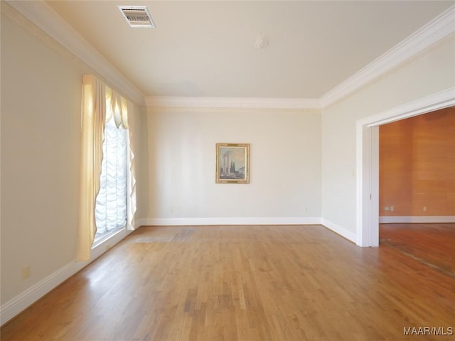 spare room with crown molding, wood finished floors, visible vents, and baseboards