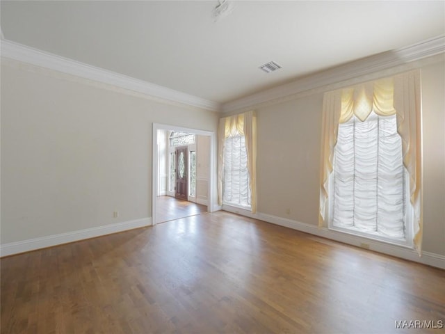 spare room featuring crown molding, baseboards, visible vents, and wood finished floors