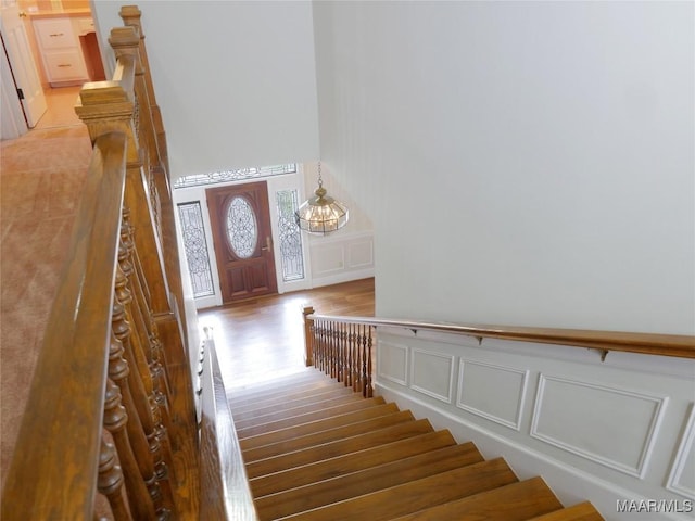 stairway with wood finished floors, a decorative wall, and wainscoting