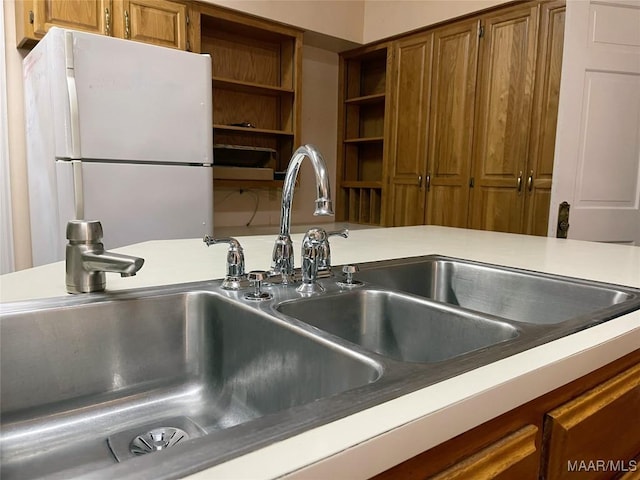 interior details with brown cabinets, a sink, freestanding refrigerator, open shelves, and light countertops