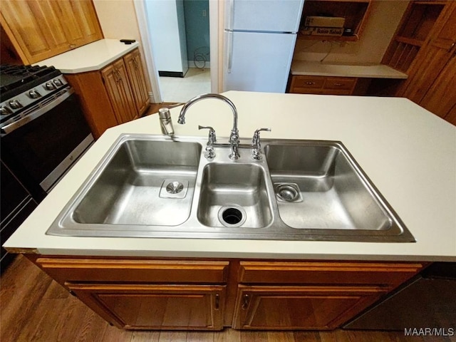 interior details featuring gas range oven, freestanding refrigerator, a sink, brown cabinetry, and light countertops