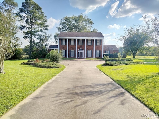 greek revival inspired property featuring concrete driveway, brick siding, and a front yard