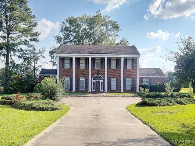 greek revival inspired property with concrete driveway, a front yard, and brick siding