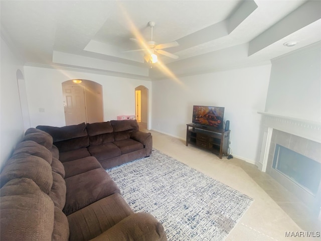 carpeted living room with ceiling fan, a tile fireplace, and a raised ceiling