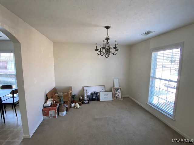 unfurnished dining area with a textured ceiling, carpet flooring, an inviting chandelier, and plenty of natural light