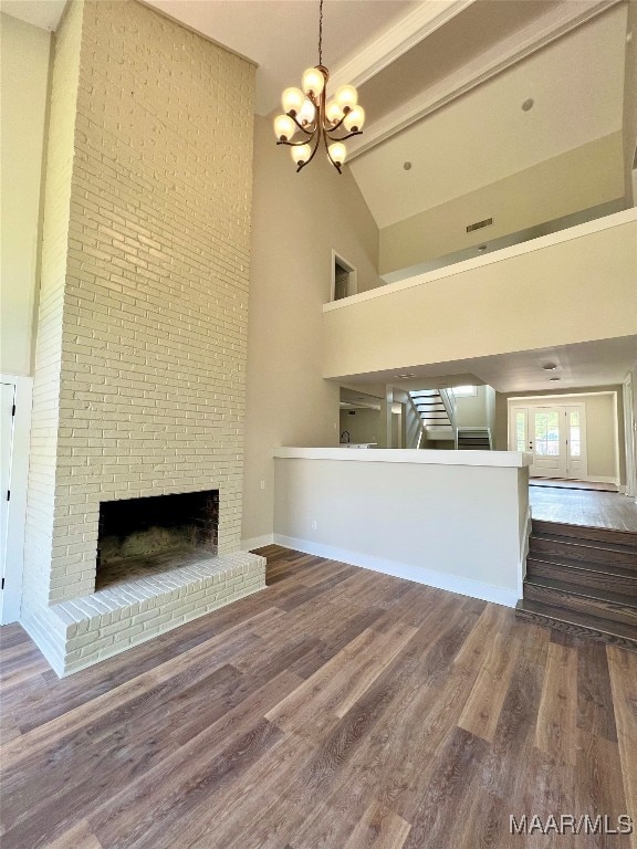 unfurnished living room featuring hardwood / wood-style flooring, high vaulted ceiling, a chandelier, and a brick fireplace