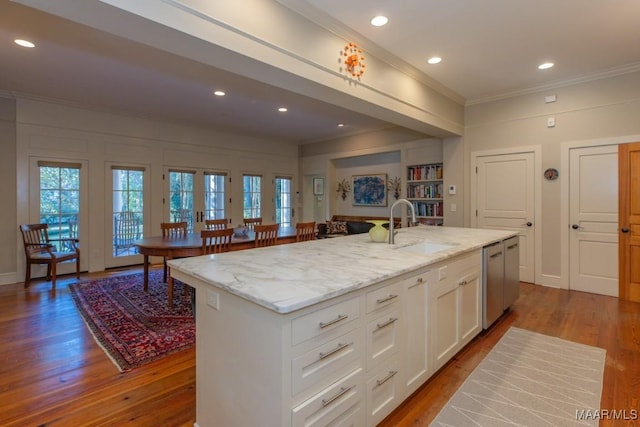 kitchen with white cabinetry, sink, light stone countertops, and an island with sink