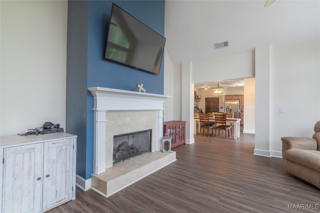 living room with dark wood-style floors, a high end fireplace, visible vents, and baseboards