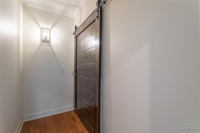 doorway featuring a barn door, baseboards, wood finished floors, and ornamental molding