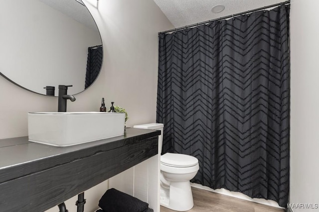 bathroom featuring sink, toilet, a textured ceiling, curtained shower, and wood-type flooring