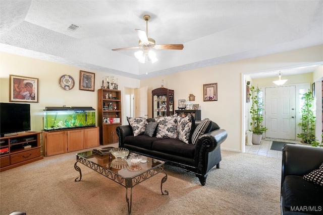 carpeted living room with a textured ceiling, ceiling fan, and a raised ceiling