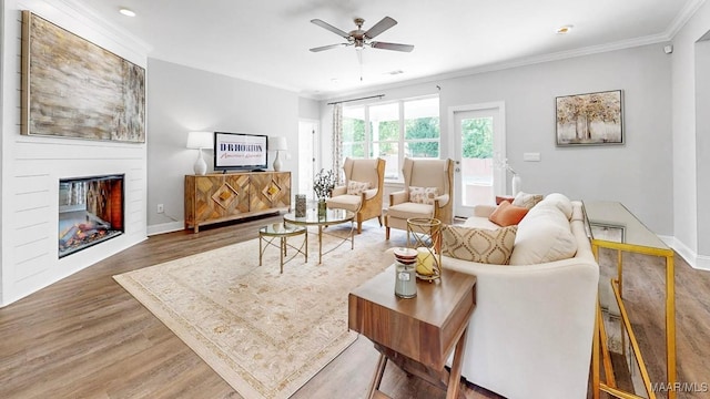 living room featuring ornamental molding, a large fireplace, ceiling fan, and dark wood-type flooring