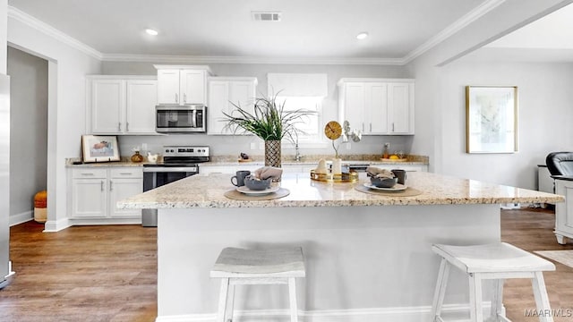 kitchen with a breakfast bar, stainless steel appliances, white cabinets, and light hardwood / wood-style flooring