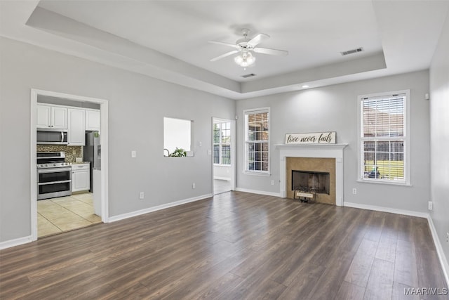 unfurnished living room featuring hardwood / wood-style flooring, ceiling fan, a raised ceiling, and a wealth of natural light