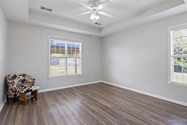 empty room with dark wood-type flooring, a tray ceiling, and ceiling fan