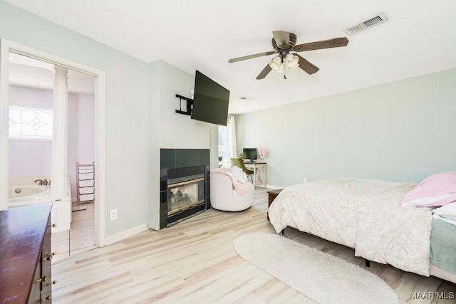 bedroom featuring light hardwood / wood-style flooring, a tile fireplace, decorative columns, and ceiling fan