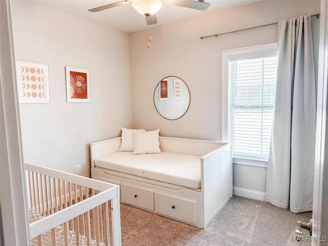 carpeted bedroom with a crib and ceiling fan