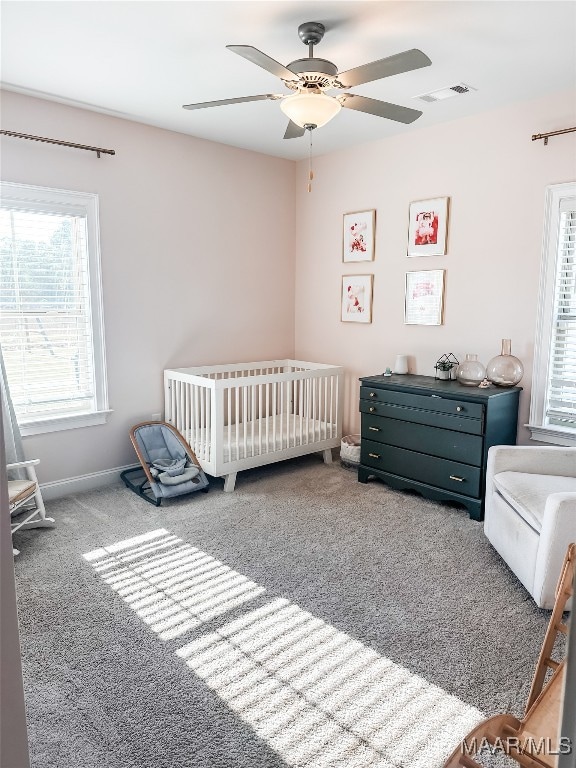 carpeted bedroom with ceiling fan and a nursery area