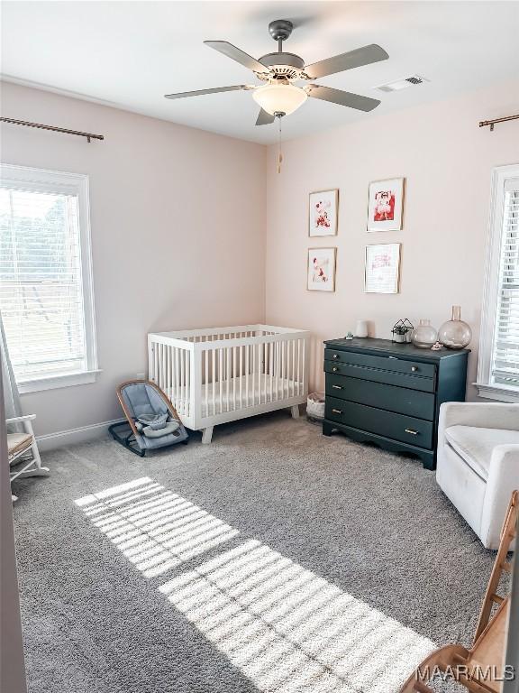 bedroom with visible vents, carpet flooring, a nursery area, and multiple windows