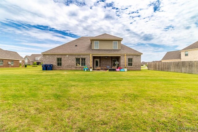 back of property featuring brick siding, fence, and a yard