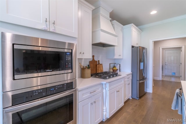 kitchen featuring custom range hood, ornamental molding, light wood-type flooring, white cabinetry, and appliances with stainless steel finishes