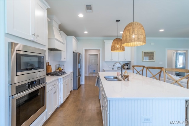 kitchen with sink, hanging light fixtures, stainless steel appliances, white cabinets, and custom range hood