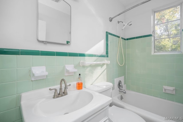 full bathroom with toilet, tiled shower / bath, vanity, and tile walls