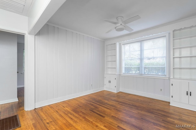 unfurnished room with ornamental molding, ceiling fan, built in shelves, and dark hardwood / wood-style flooring