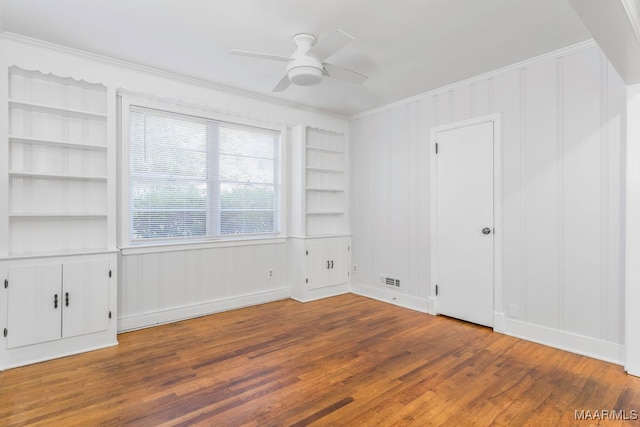 empty room with crown molding, ceiling fan, built in shelves, and dark hardwood / wood-style flooring