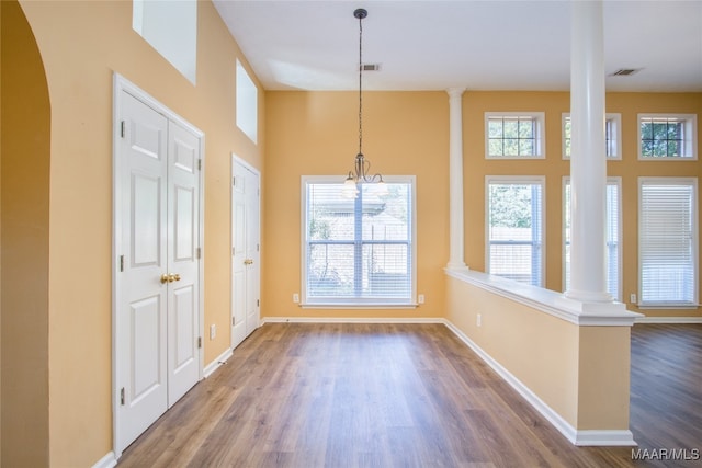 unfurnished dining area with hardwood / wood-style flooring, decorative columns, and a high ceiling